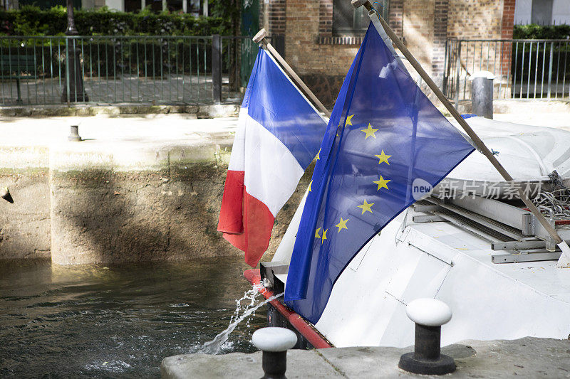法国国旗和欧盟旗帜在一艘通过运河水闸的内河船的背后