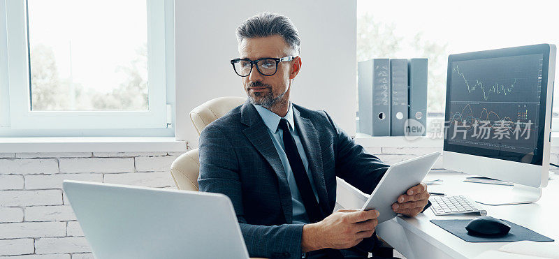 英俊成熟的男人穿着正装，坐在办公室里使用科技产品