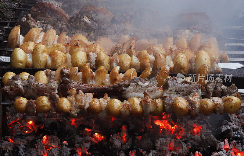 把土豆和培根串在金属串上，放在热炭上烤。特写镜头
