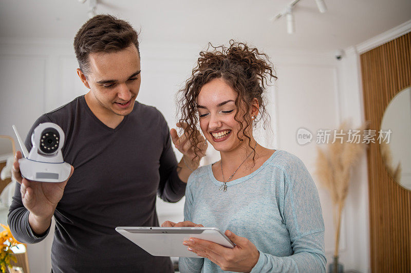 一对年轻夫妇，一男一女，正在他们的公寓里安装家庭监控摄像头