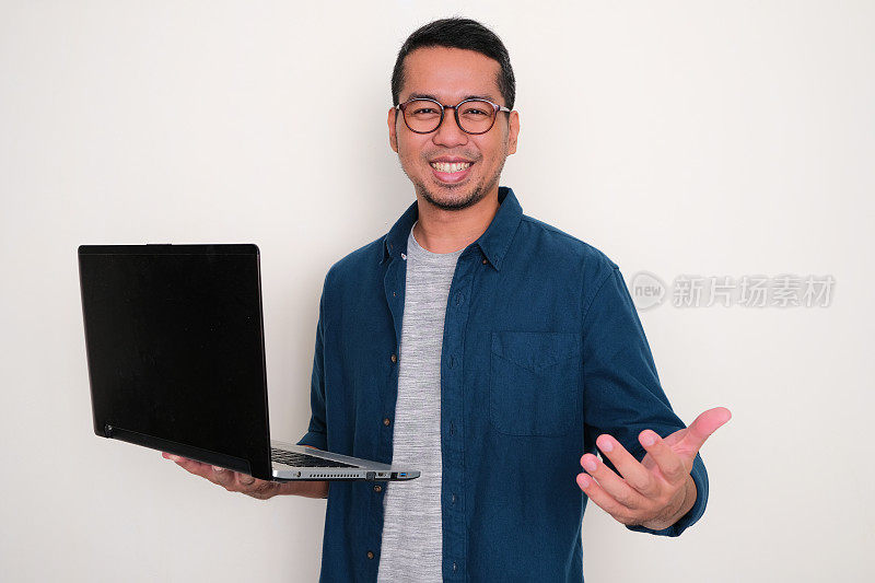 成年亚洲男子微笑快乐，同时拿着笔记本电脑