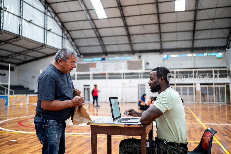 一名士兵在难民避难所使用笔记本电脑与一名残疾难民交谈