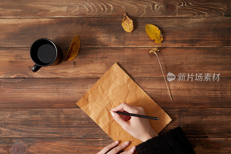 在白纸上写字。木制背景与一杯咖啡和秋叶。