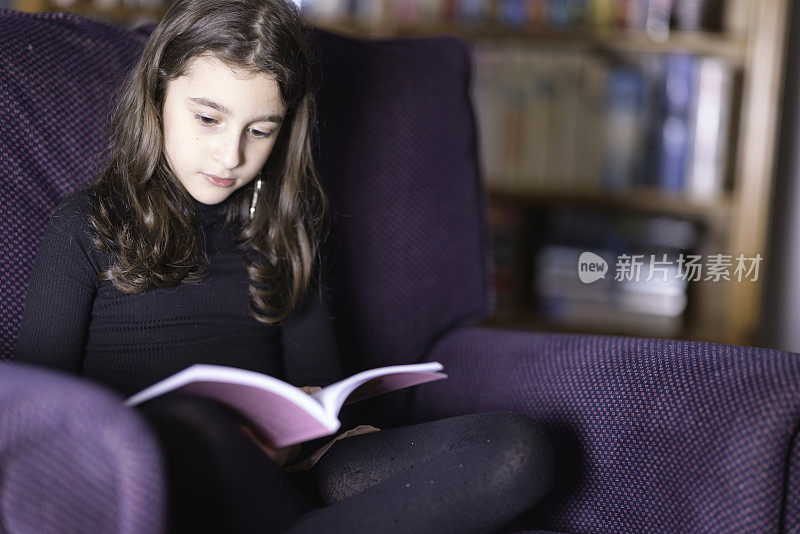 小女孩坐在扶手椅上看书