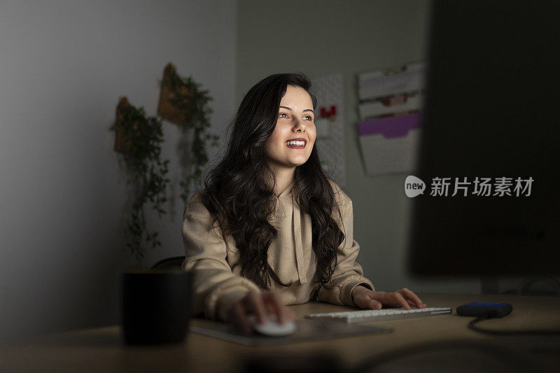 女性坐在家庭办公室的办公桌前，用笔记本电脑工作到深夜;在家远程加班的女性网页设计师