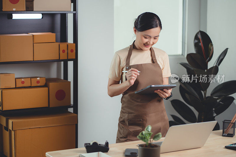 亚洲女性在线卖家使用平板电脑在家庭办公室检查产品库存。