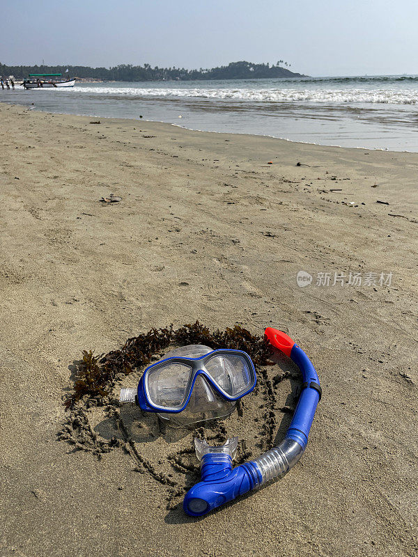 在海滩沙滩海岸线上绘制的头部图像，由海藻形成的头发，水肺面罩和通气管，低潮时水的边缘打破波浪，海洋背景，重点在前景，复制空间