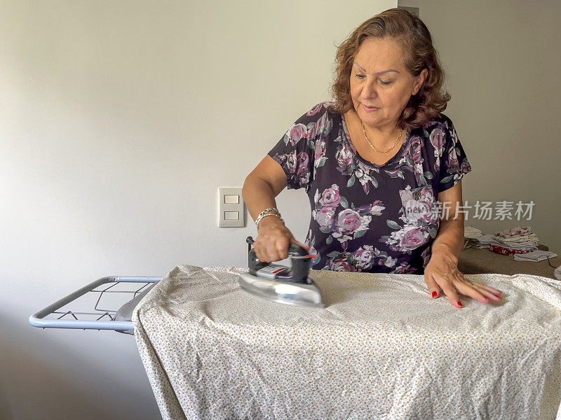 西班牙裔老年妇女在家熨衣服