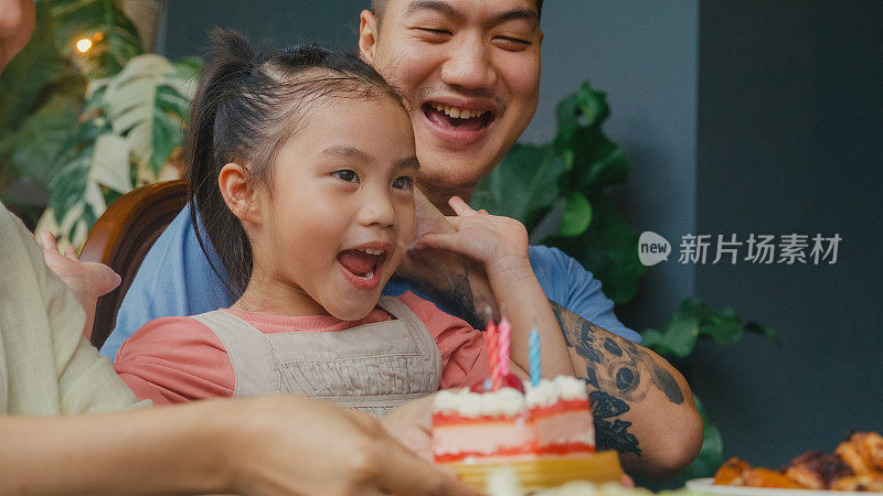 亚洲家庭吹生日蜡烛在蛋糕上，而庆祝和乐趣坐在餐桌上在家外面的后院。多代同堂的家庭一起享受消费。