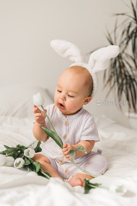 可爱的宝宝头上戴着兔子耳朵，家里的床上放着郁金香。复活节和春天