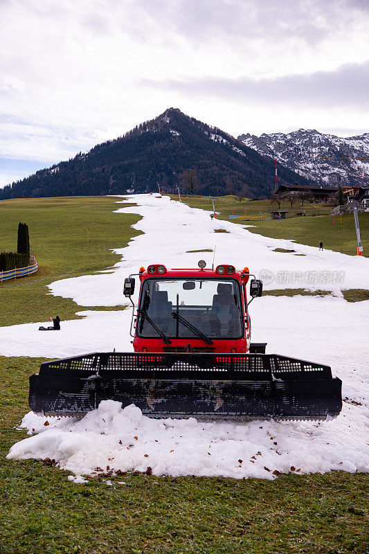 一辆雪车(雪猫、雪道机或雪道修理工)正在准备在奥地利蒂罗尔沃尔什的滑雪场准备滑雪道。一个滑雪道和一个滑雪缆车(t型缆车)在背景中。