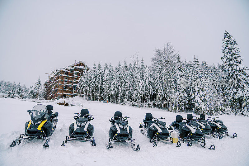 一排雪地摩托停在滑雪胜地小山上森林边缘的雪地上
