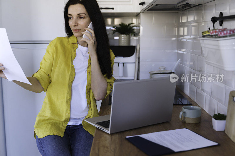 一个女人早上在厨房吃早餐时使用笔记本电脑。