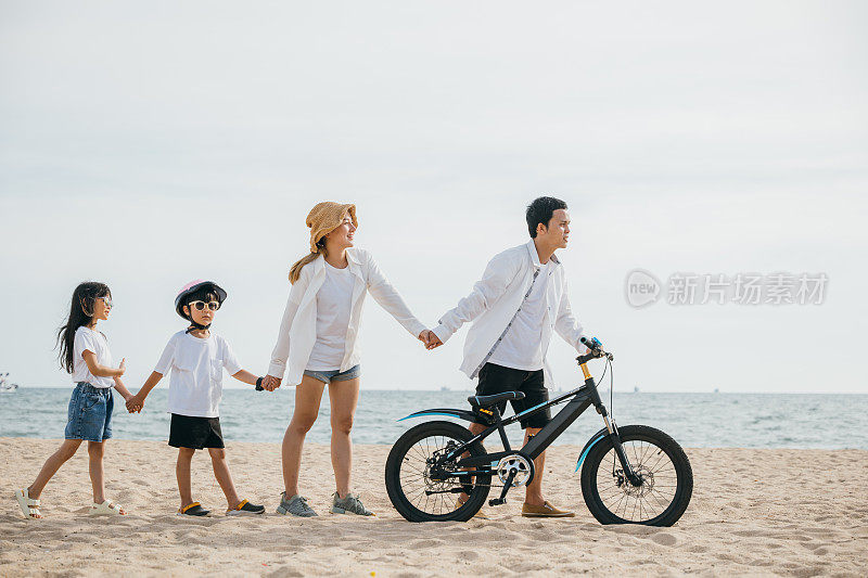一个风景如画的家庭漫步在海滩上，父母推着自行车，充满了幸福快乐和童年无忧无虑的精神，创造了一个鼓舞人心的海上场景。一家人去海滩度假