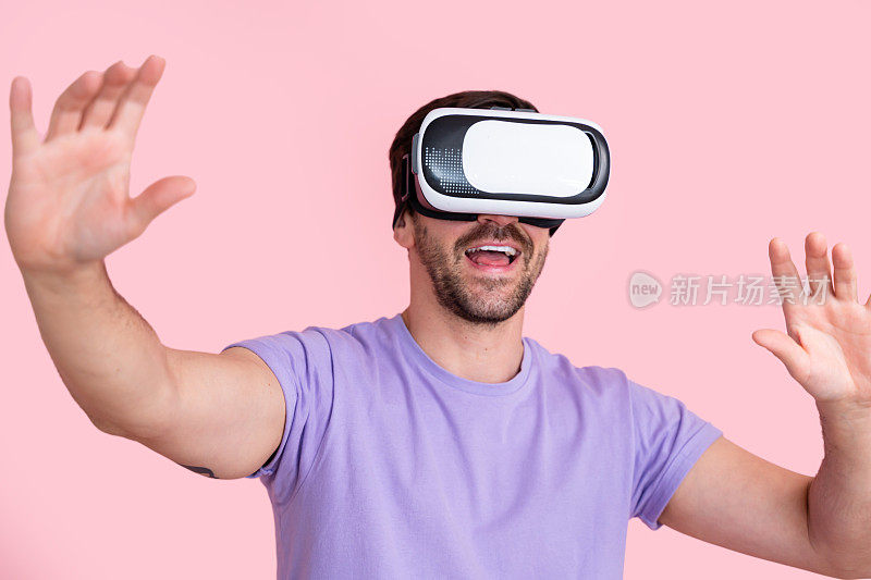 年轻的成年男性戴着粉色背景的虚拟现实耳机，微笑着伸出手，沉浸在虚拟体验中