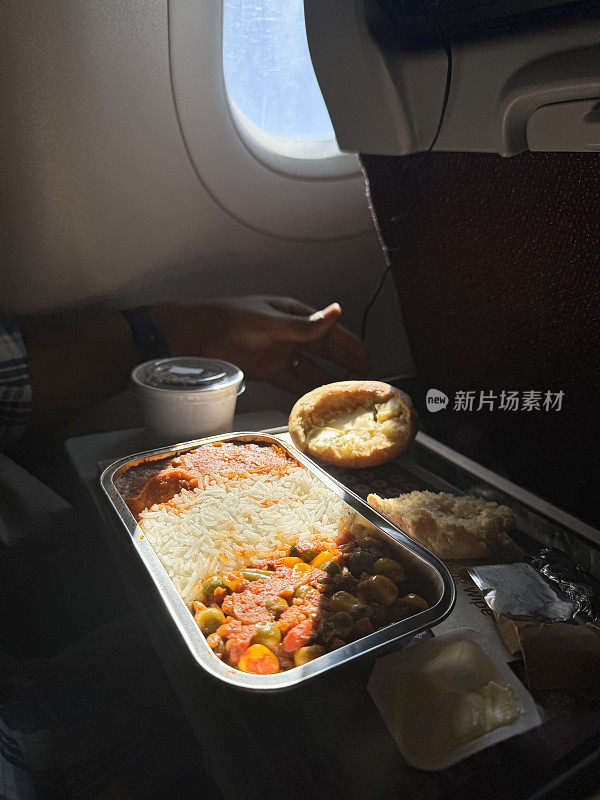 飞机餐盘的图片，里面有锡纸托盘里的印度咖喱饭和白米饭，白面包卷和黄油，塑料碗里的巧克力慕斯，木叉餐具，高架视图，重点在前景