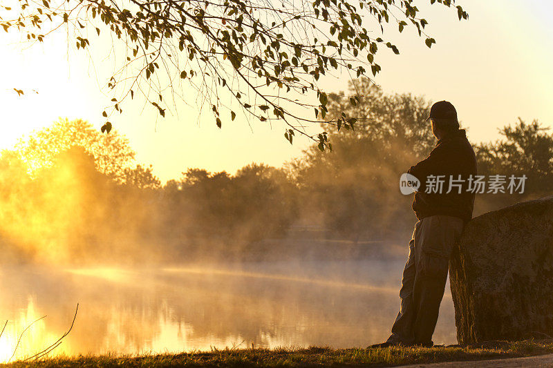 成年男性独自站在日出，凝视着雾蒙蒙的湖