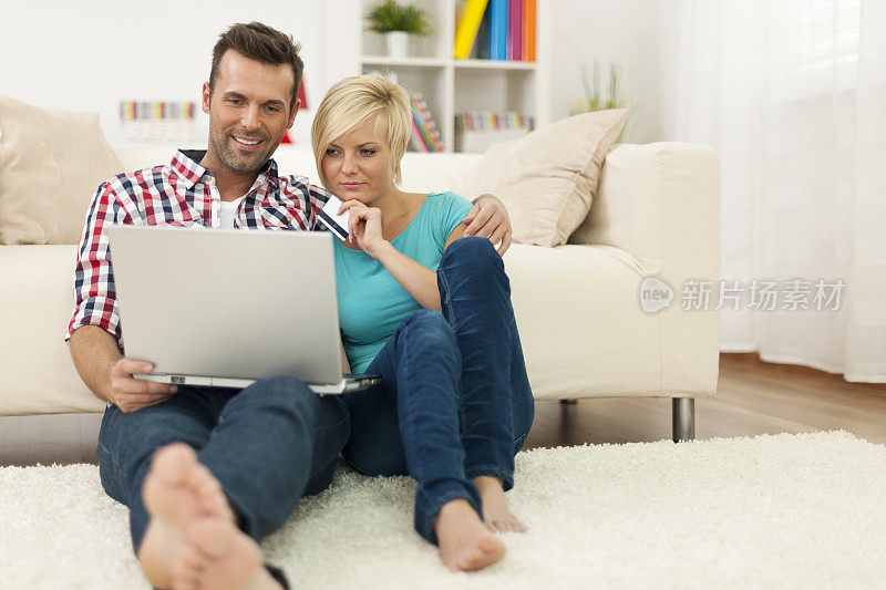 一对夫妇坐在家里的地毯上，在网上购物