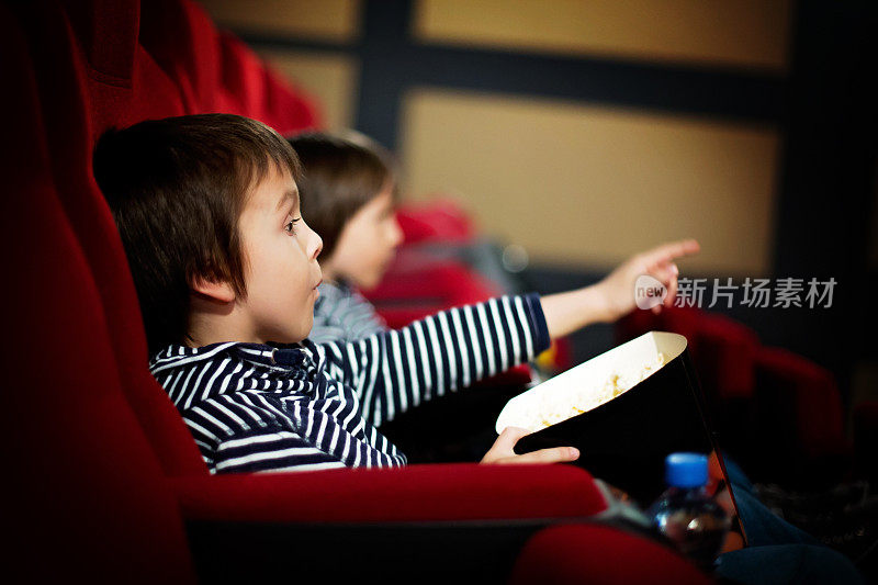 两个学龄前的孩子，双胞胎兄弟，在电影院看电影，吃爆米花