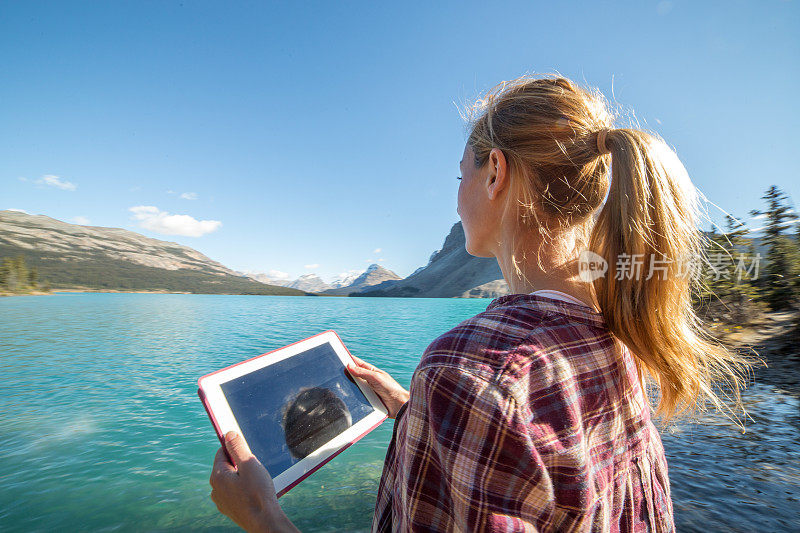 年轻女子在湖边用平板电脑拍摄风景