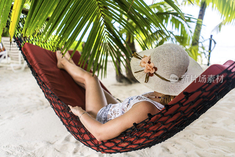 戴着太阳帽的女人在沙滩吊床上休息。
