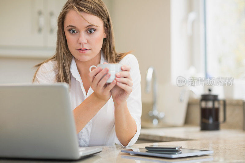 女人一边喝茶一边用笔记本电脑工作