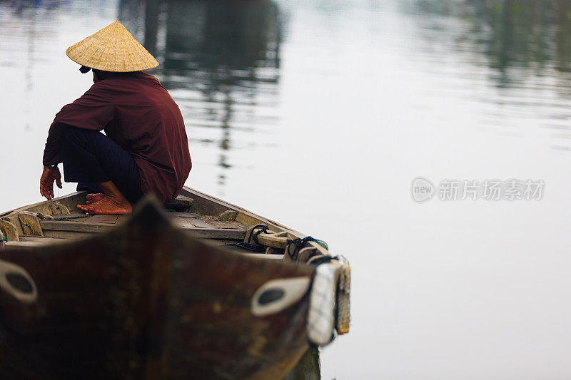 戴着传统帽子坐在船上的越南老人