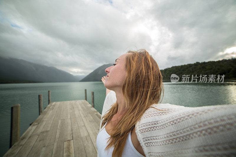 一个年轻女子的肖像在湖码头上张开双臂