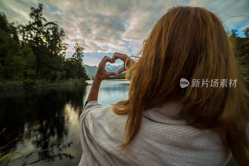 女人在山湖景观上做心形指架