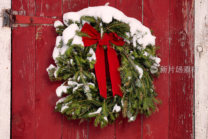 红色谷仓门上的圣诞花环，新鲜的雪