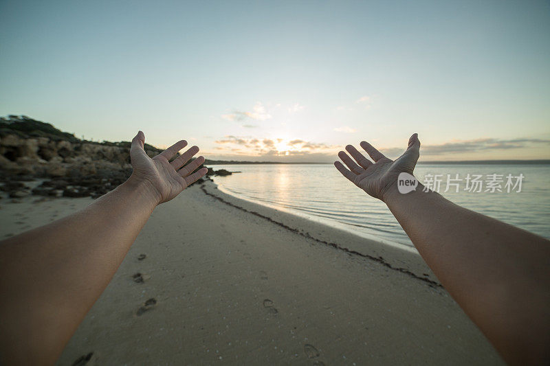 女人的双臂伸向海面上的夕阳