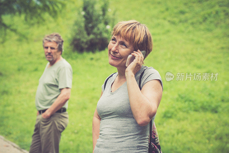 一对年长白人夫妇在户外，一个女人在用智能手机聊天
