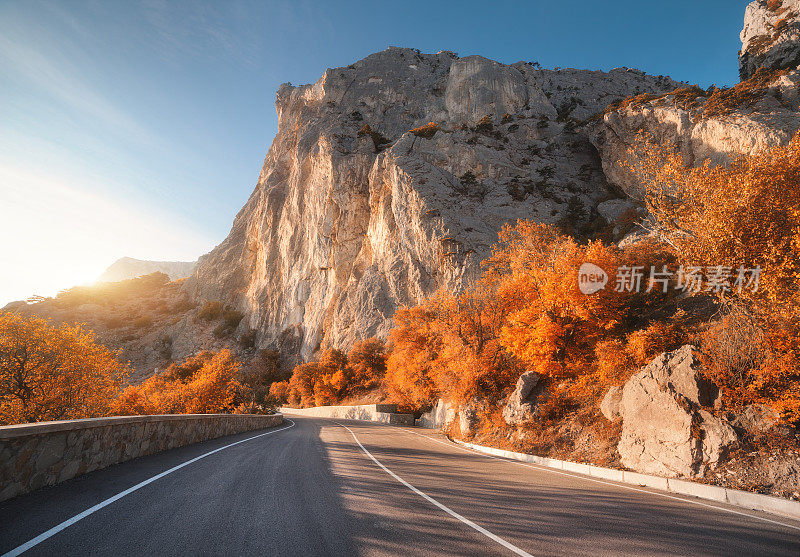 秋天日出时的柏油路。风景优美，空旷的山路上有完美的沥青，高高的岩石，树木和阳光灿烂的天空。古董塑身。旅游的背景。在山区高速公路。速度