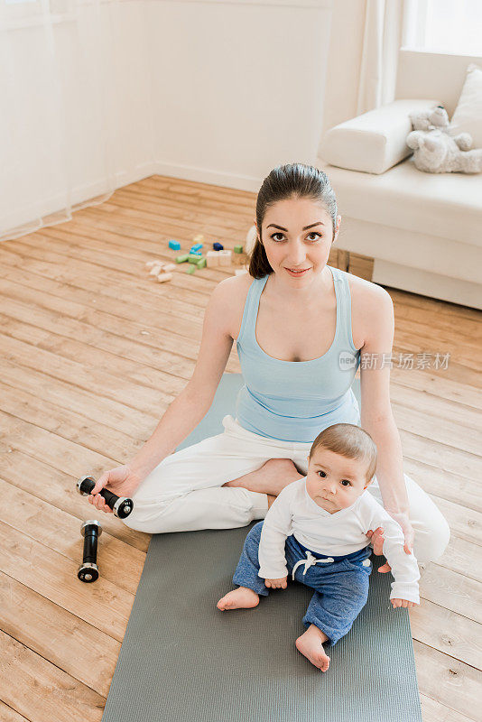 女人和婴儿坐在瑜伽垫上，手里拿着哑铃
