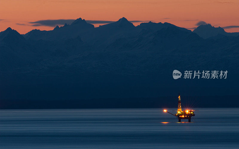 水上石油平台在日落与灯光和山脉的背景，阿拉斯加