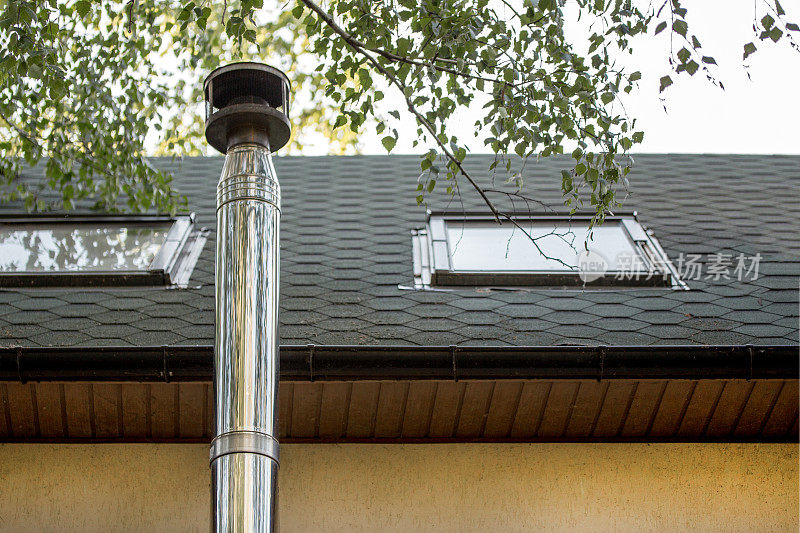不锈钢烟囱烟道上的瓦片覆盖的屋顶与窗户在乡村别墅