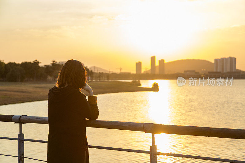 年轻女子在公园人行桥上欣赏美丽的日落风景