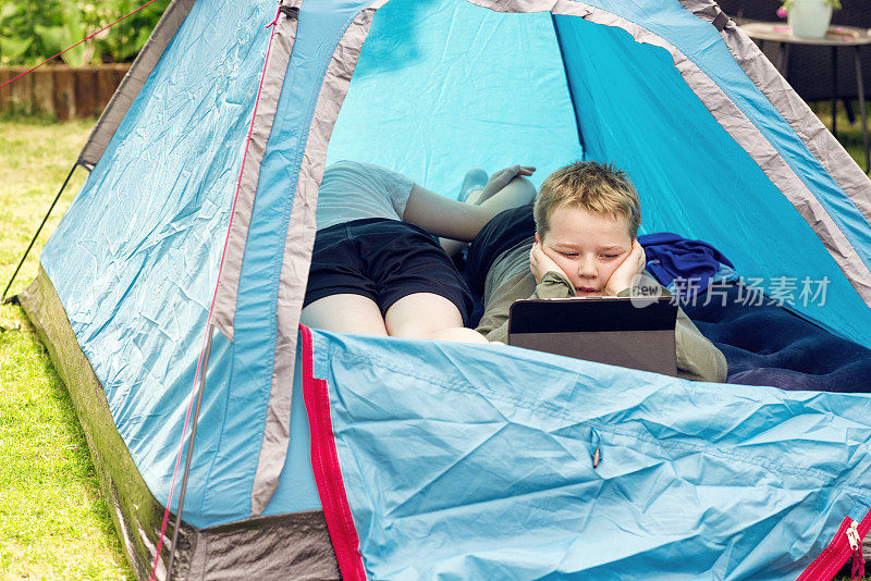 男孩在外面的帐篷里休息，在数字平板电脑上无线观看内容
