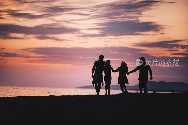 黄昏时分，四个朋友在海滩上散步的剪影。