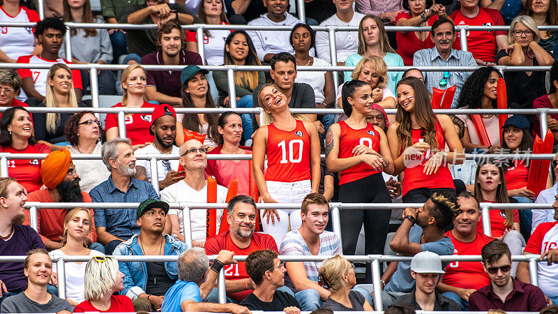 三个穿着红色衣服的漂亮女人在体育场的人群中欢呼