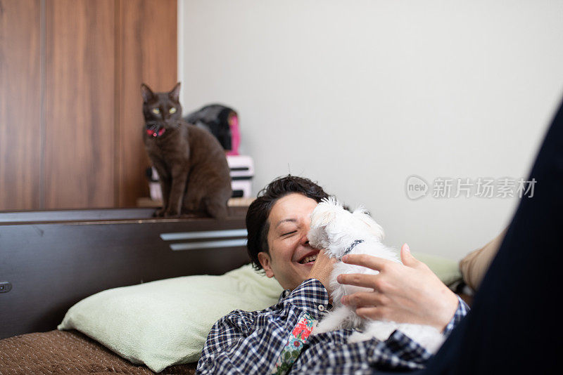 男人在床上抱着小狗，猫坐在床角上