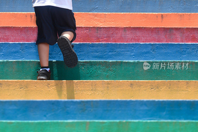 下半身一个男孩穿着休闲鞋走上户外多彩的楼梯，孩子的生活方式成功理念