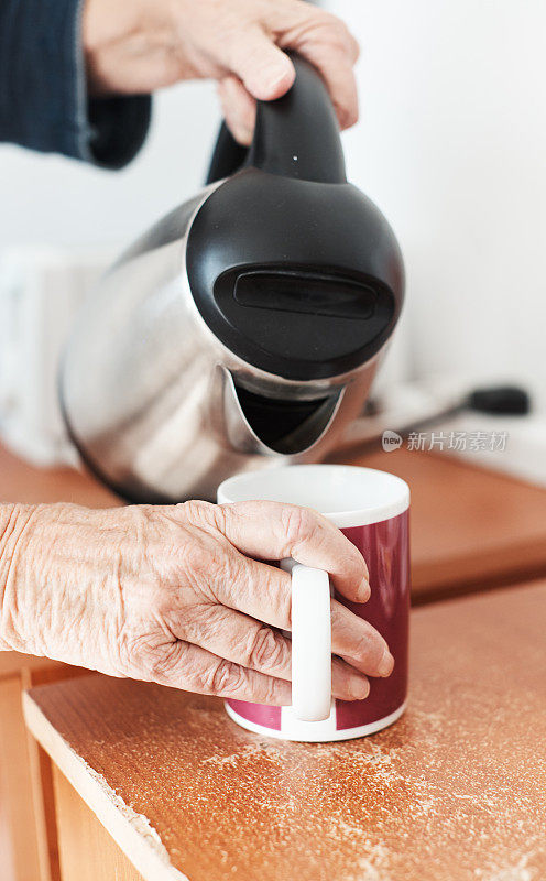 年长的妇女把水壶里的水倒进马克杯里泡茶或咖啡