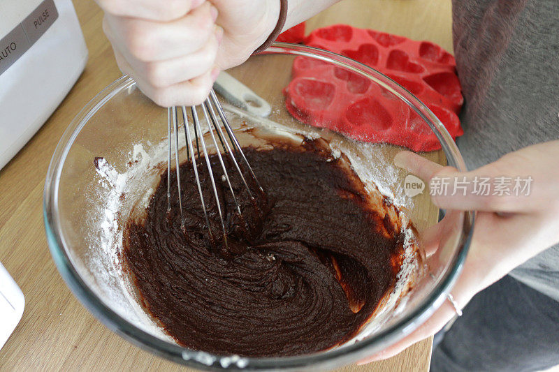自制巧克力维多利亚海绵蛋糕的图像，黄油，糖，面粉和可可混合在玻璃厨房搅拌碗中，木制的厨房工作台