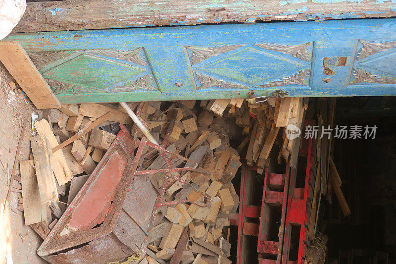 图片显示不整洁的储藏室，红色的木托盘，成堆的锯木材和木块与倒置的，生锈的手推车