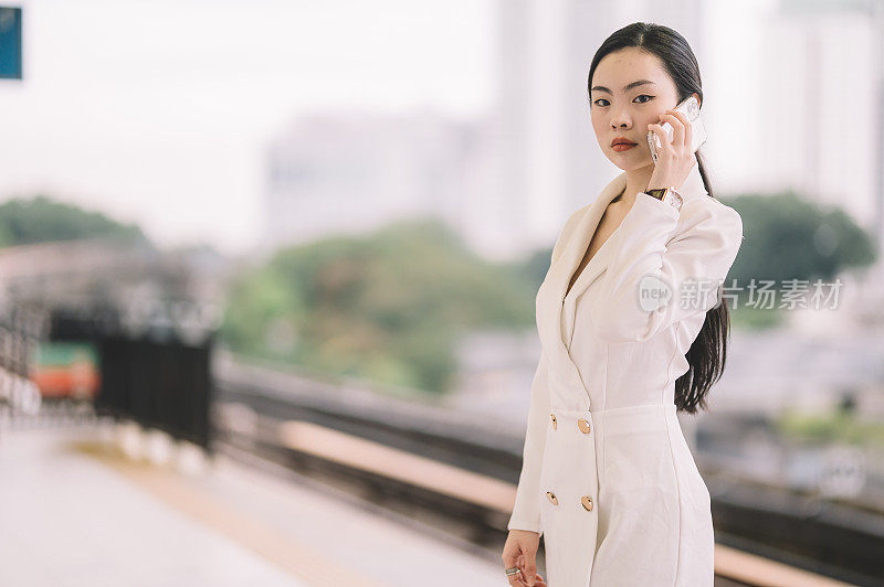 一位年轻的亚洲华裔女商人在单轨火车站边走边听着智能手机