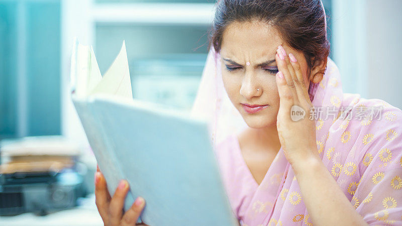 一名紧张的年轻女子一边看书，一边抬起头来摆脱头痛。