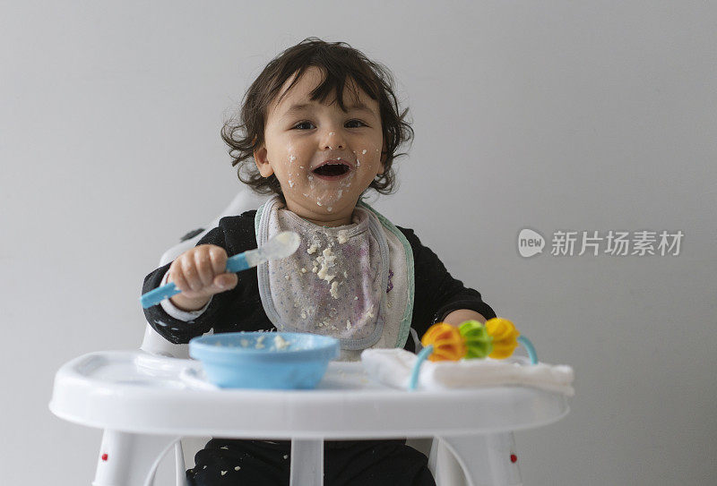 可爱的小男孩在一团乱麻中学习自食其力，坐在高高的椅子上