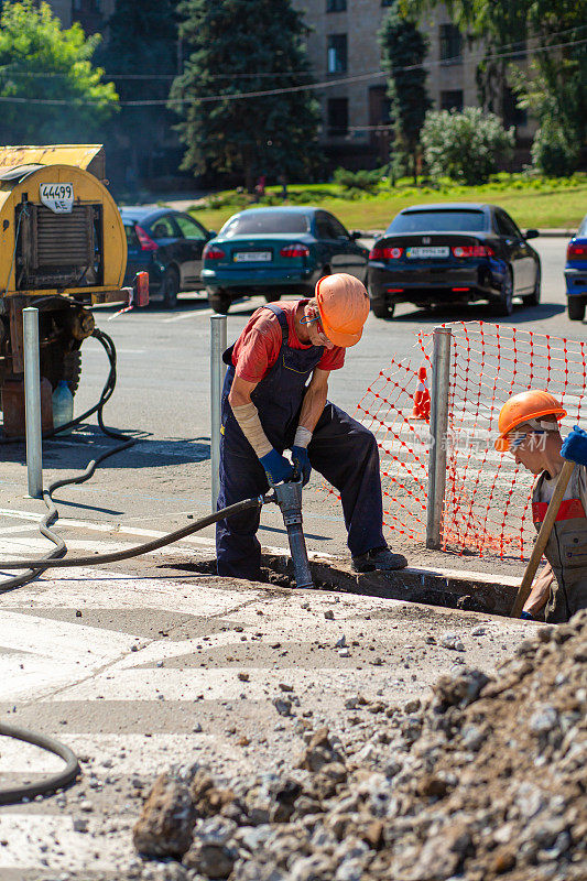 城市街道的维修工作。专业工人用专业工具拆除部分道路。工人们除去沥青并挖一个洞。技术专家，工作流程在城市街道上。