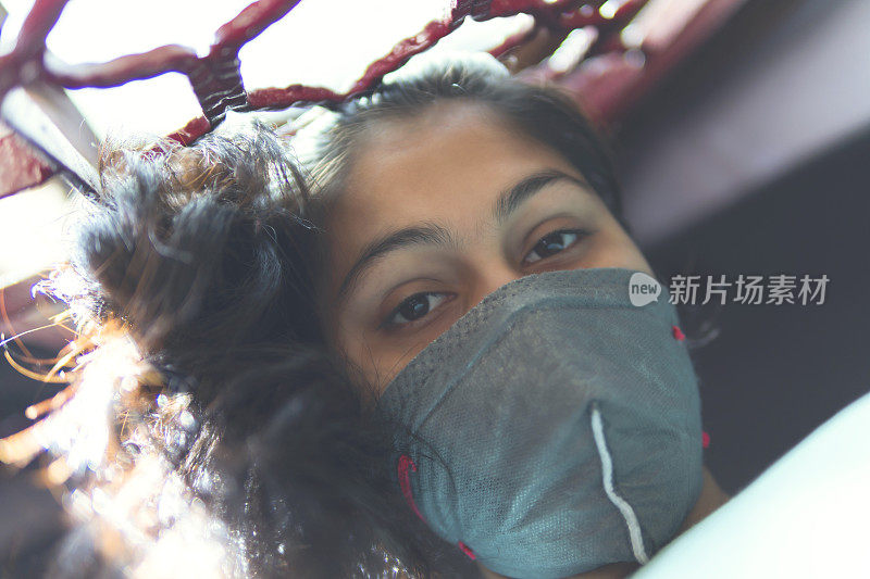 这个悲伤的女孩正在保护自己，戴着口罩，在家里自我隔离。